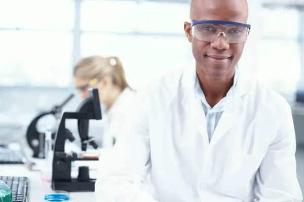 The science guy. Portrait of a smiling young chemist in the lab with a female coworker in the background