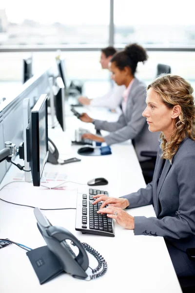 Focused on delivering excellent work. Profile view of a serious businesswoman working on her computer with her colleagues in the background