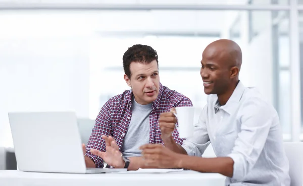 Partners on a new project. Two professionals having a work discussion while seated at a desk with a laptop