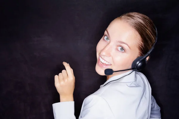 Pretty business woman with a headset on black , copyspace. Happy young business executive with a headset isolated against black background
