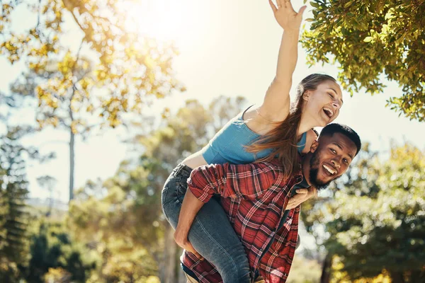 Diverse, couple and piggyback fun with a man and woman having fun in nature during summer. Adventure, happy couple and interracial people in a green garden or natural environment with happiness.