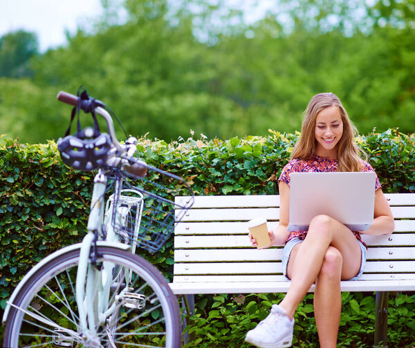 Inspiration strikes at any time. a young woman using a laptop on a bench while out for a cycle in the park
