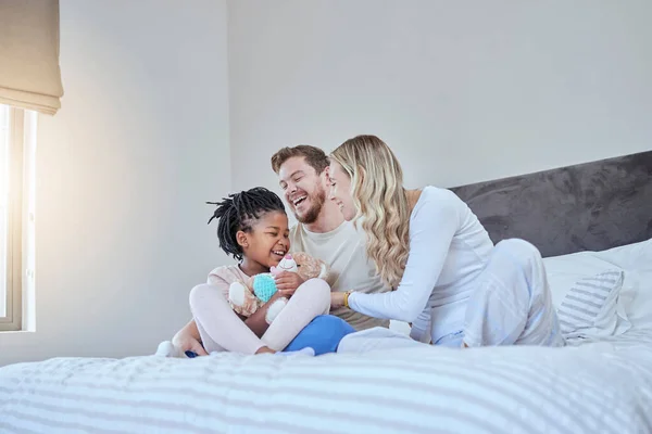 Interracial, adoption family and bed with smile, happiness and bonding together with kid, home and love. Diversity, happy family and sitting in bedroom with child, african girl and parents in house.