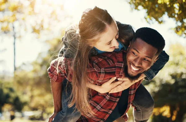 Love, piggy back and couple in park walking, smile and happy together, for bonding and outdoor. Romantic, interracial man and woman or loving on spring vacation, holiday and romance for relationship.