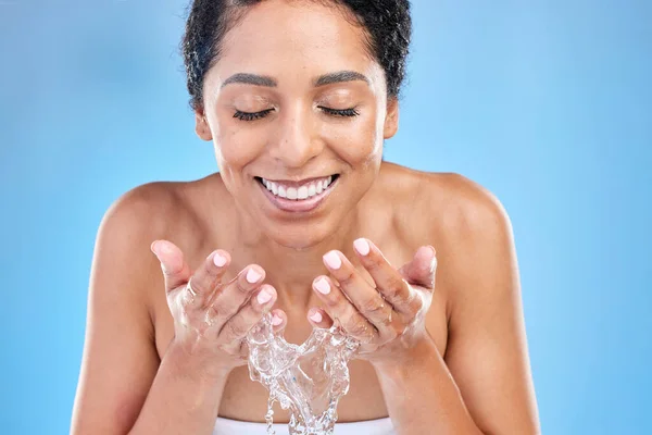 Splash, water and black woman for facial skincare, cleaning or healthy glow promotion on blue studio mockup. Beauty, skin care and cosmetics model with water splash in her hands for natural face wash.