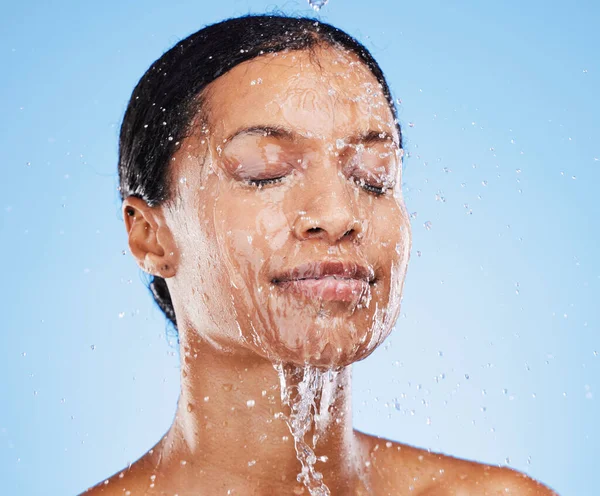 Woman, shower and water splash on face for skincare hydration or clean hygiene against blue studio background. Female in facial wash with water to hydrate or cleanse for hygienic body care treatment.