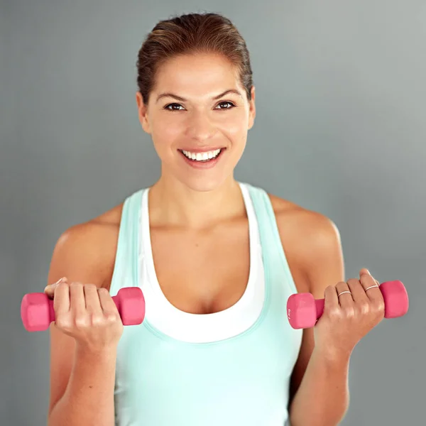 Sweat now, smile later. a young woman working out with dumbbells against a gray background