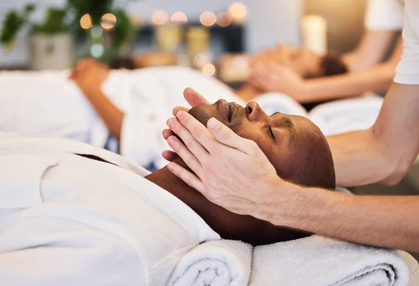 Face massage, beauty therapist and black man, skincare and relax in luxury spa with zen, hands and rest on a bed. Wellness, skin health and cosmetic treatment for healthy skin and relaxing body.