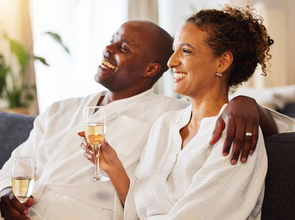 Black couple, champagne and spa therapy on a couch to relax, celebrate and feel zen while together at a hotel for hospitality. Man and woman, happy while drinking alcohol and enjoying quality time.