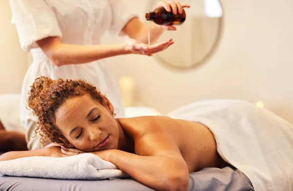 Spa, luxury massage and woman with essential oil getting back massage for wellness in beauty salon. Health, beauty and black woman with massage therapist for relaxation, stress relief and body care.