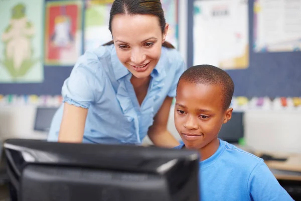 Teaching her students about computer technology. An attractive young woman helping out a young ethnic boy in computer class
