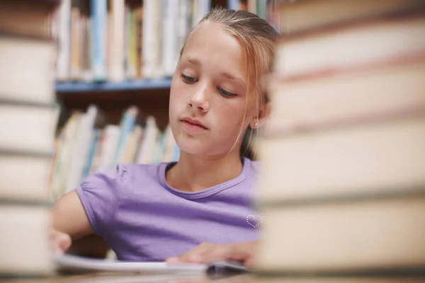 被一个好故事吸引住了一个可爱的小女孩在图书馆边读书边做功课 — 图库照片