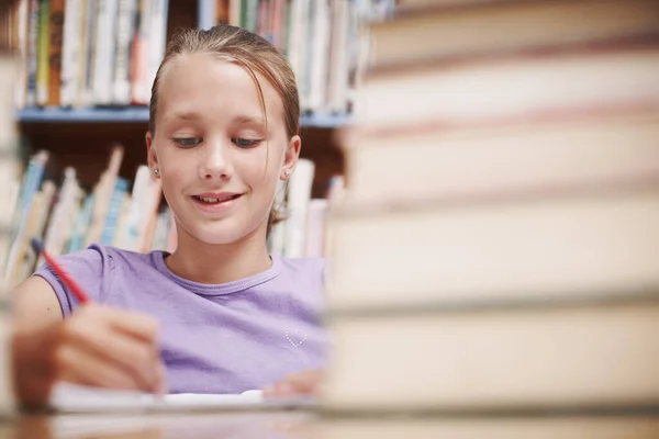 她喜欢写作 一个年轻可爱的女孩坐在图书馆里进行创造性的写作 — 图库照片