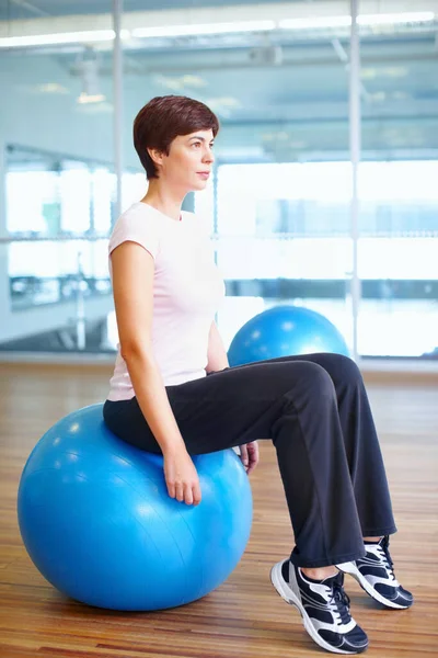 Planning workout routine. Full length of woman sitting on exercise ball and planning her next workout routine