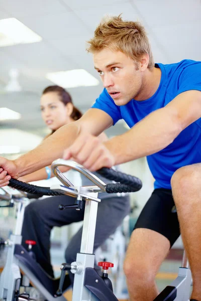 Body conscious. Young man exercising with spinning bicycle at gym