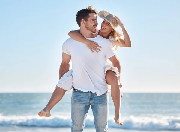 Love, couple and piggy back at beach on vacation, holiday or summer trip outdoors. Romance, support and happy man carrying woman on shoulders, enjoying quality time together or having fun at seashore.