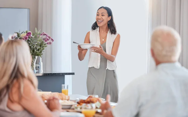 Woman, excited and serving family at thanksgiving dining table in house or home for celebration event, holiday or buffet party. Smile, happy or festive person with healthy food, meal or brunch bowl.