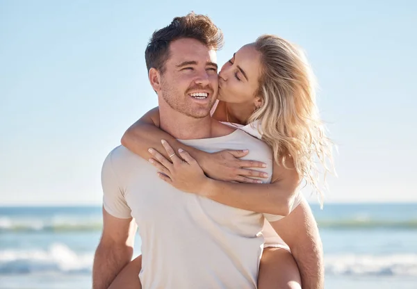 Beach love, hug and couple kiss on romantic date, bonding getaway or outdoor nature adventure for peace, freedom and fun. Ocean sea, blue sky and man and woman piggyback on Sydney Australia holiday.