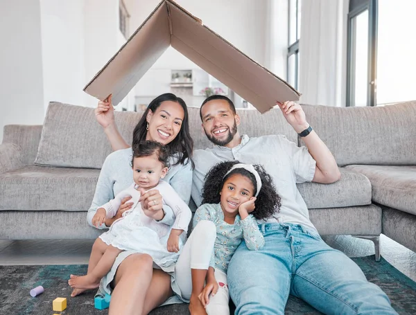 Family, cardboard roof with home insurance and together in house, love in portrait, unity with mortgage and happy family. Parents, children on living room floor, cover with protection and property
