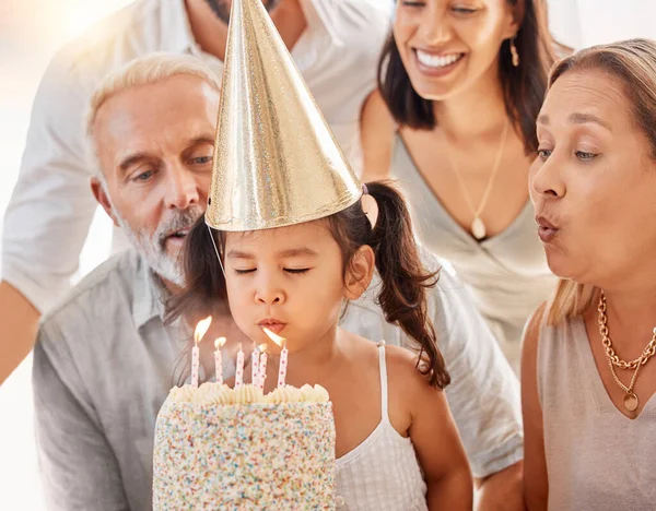 Blowing candles, birthday cake and happy family with a girl to celebrate with a wish, food and eating at a birthday party. Happy birthday, smile and kid with parents and grandparents at a celebration.