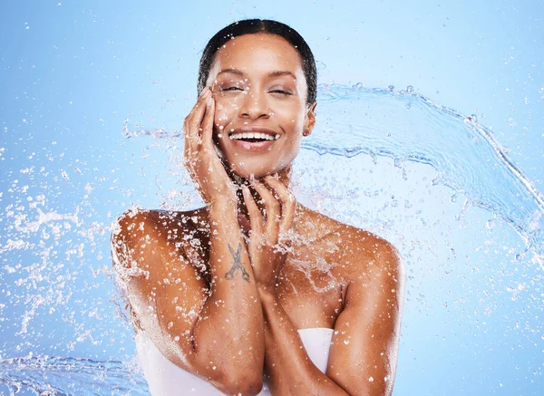 Water splash, woman and skincare for beauty, moisturizer or hydration by blue background wall. Black woman, skin model and splashes for cosmetics, health or dermatology wellness by cosmetic backdrop.