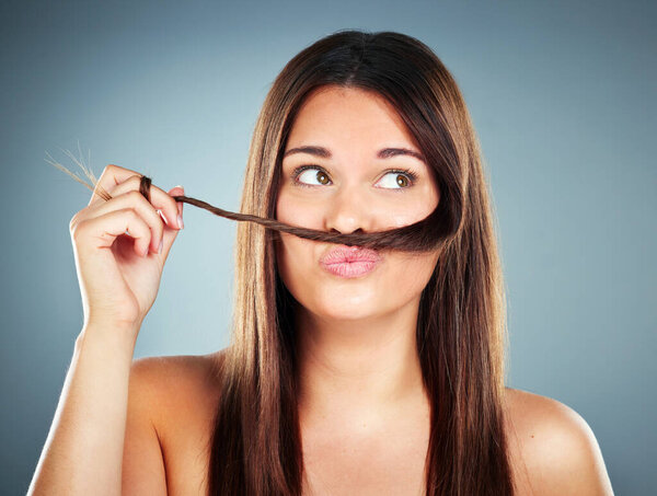 Woman, hair and face of a female with a braid and silly face expression for haircare on a grey studio background. Beauty, cosmetology and brunette with a hair moustache for comic face with hairstyle.