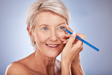 Yüz, güzellik ve göz kalemi. Stüdyoda yaşlı bir kadın var. Kozmetik için gri arka planda. Makyaj, güzel ve göz kalemi ve yüzüne kozmetik ürün uygulayan olgun bir kadın..