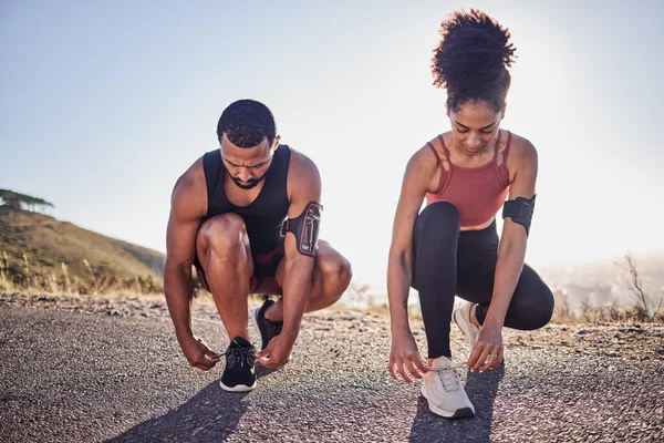 Fitness couple, running shoes and exercise on a road outdoor for cardio workout and training together for health and wellness. Black woman and man tying shoelace or sneakers for a agile run.