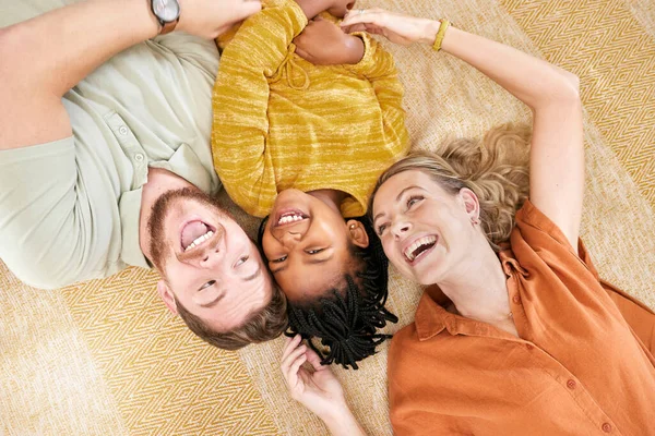 Interracial family, adoption and home on floor with head together for love, happy and bonding. Mom, dad and african girl child lying with smile, happiness and diversity on carpet with top view.