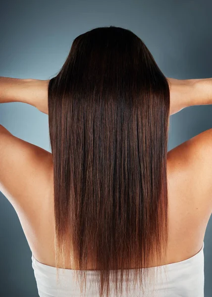 Hair, beauty and keratin treatment with a model woman in studio on a blue background for wellness or haircare. Head, product and salon with a female posing to promote nature haircare from the back.