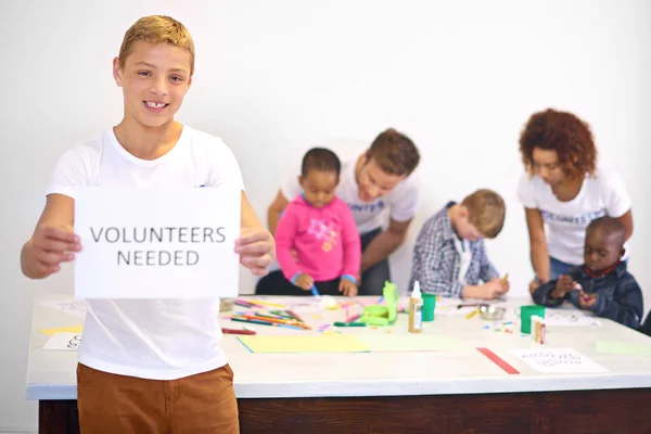 我们总是需要更多的帮助之手 需要与背景中从事幼儿工作的志愿者签名的志愿者手持志愿者的肖像 — 图库照片