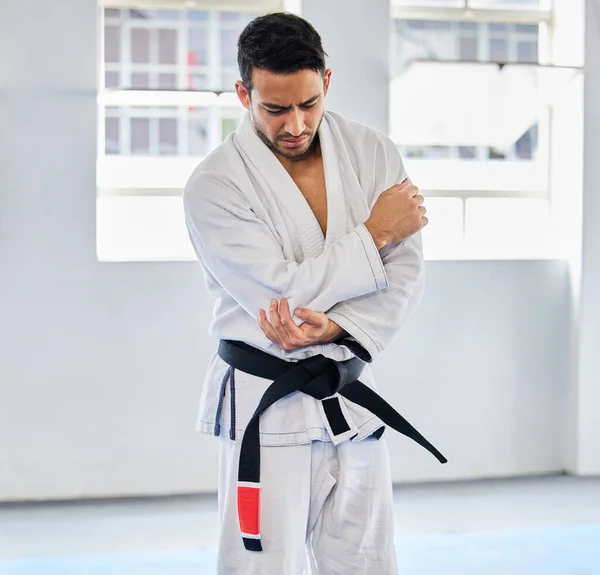 Karate, arm pain and man with injury in dojo, healthcare and fighting. Sports, fitness and martial arts fighter in India with hand elbow sports injury and medical emergency in fighting gym or studio
