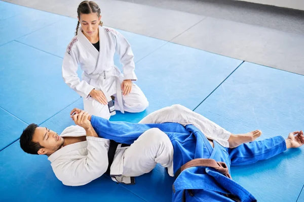 Karate, personal trainer and self defense training in the dojo for physical protection or health and safety. Black belt sensei man teaching woman to defend herself in a fight or combat at the gym.