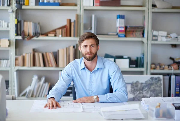 Architecture is his passion. Portrait of a handsome young architect sitting at his desk with blueprints in front of him