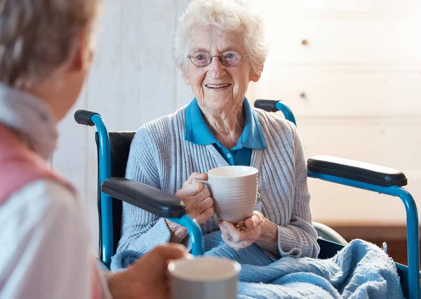 相談医療会話の中で朝コーヒーを飲む高齢者 車椅子 女性患者 移動障害 老人ホーム女性介護者の看護師と話す幸せ — ストック写真
