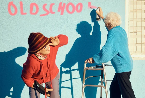Senior women, friends and spray paint for vandalism, graffiti and street art to spray old school on nursing home building wall and keep watch. Crazy old people break law with illegal activity outdoor.