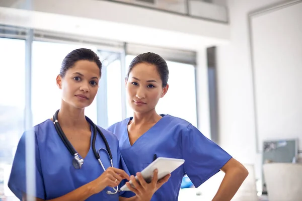 Nursing is a serious business. Portrait of two female nurses standing with a digital tablet in a hospital