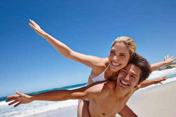 夏は楽しい時間です 彼のガールフレンドにビーチでピギーバックに乗ってもらうと — ストック写真