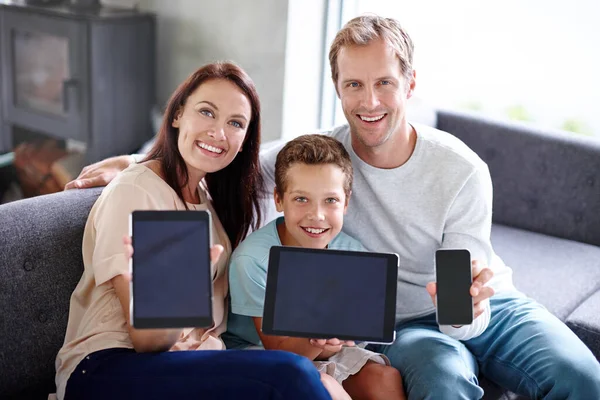 Check out our family tech. Portrait of a happy family holding up their tablets and smartphones while sitting on the sofa at home