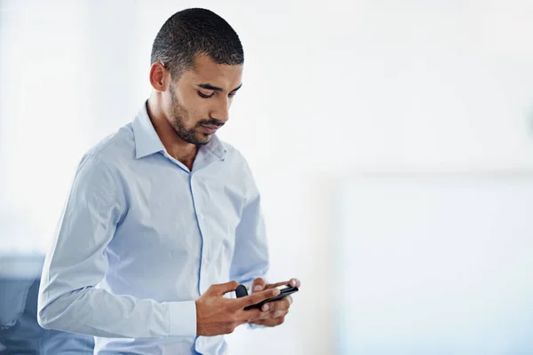 Always reachable. a young businessman sending a text message while standing in an office