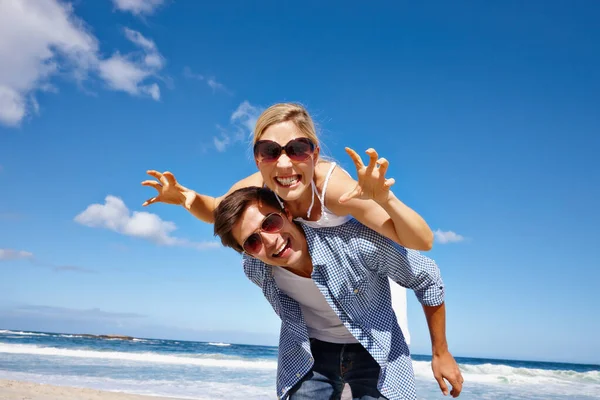 阳光的笑柄 一对快乐的年轻夫妇在海滩上享受着搭便车的乐趣 — 图库照片