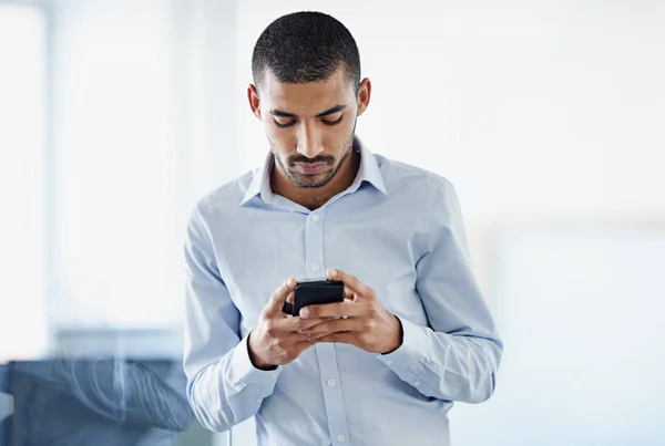 Business mobility. a young businessman sending a text message while standing in an office