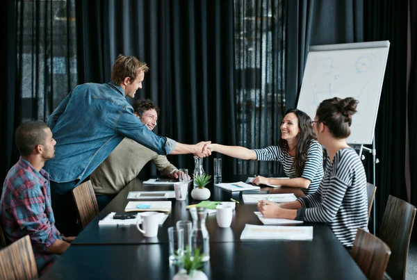 Getting deals done with a smile. two colleagues shaking hands in a boardroom while coworkers look on