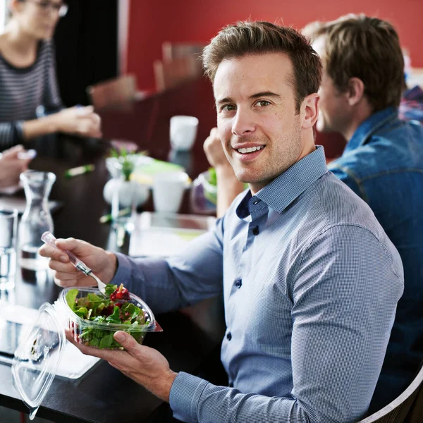 stock image We eat healthy in this office. Portrait of a young office worker eating lunch with coworkers at a boardroom table