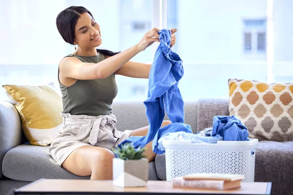 Cleaning, laundry and folding clothes with woman in living room for housekeeping, fresh and tidy. Fabric, washing and basket of linen with cleaner on sofa at home for household, chores and domestic.