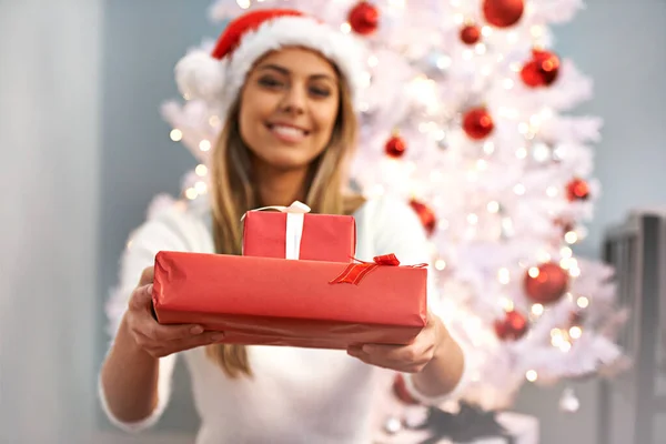 これは君のためだ クリスマスツリーに座っている間にプレゼントを保持している美しい若い女性の肖像画 — ストック写真