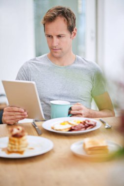 Kahvaltı yaparken etrafı kolaçan ediyorum. Evde kahvaltı yaparken tabletini kullanan yakışıklı bir adam.