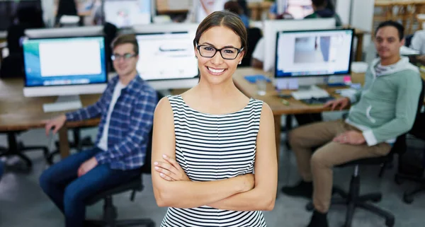 Leading her team with a positive attitude. Portrait of a smiling young designer standing in an office with colleagues working in the background