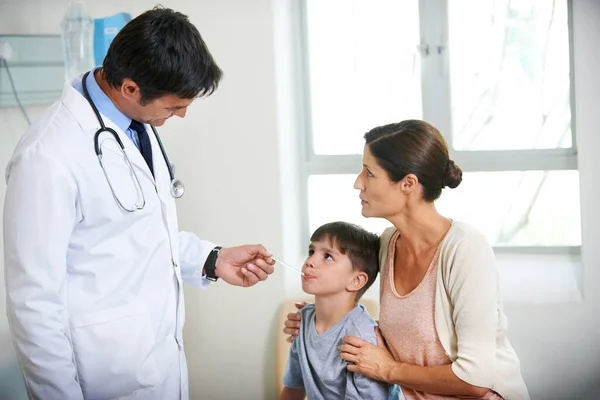 Youre going to be just fine. The family doctor takes a young boys tempreture while his mother holds him