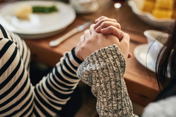 Hands, pray and family at a table for food, blessing and gratitude before sharing a meal in their home together. Hand holding, worship and people praying before eating, prayer and religious respect.